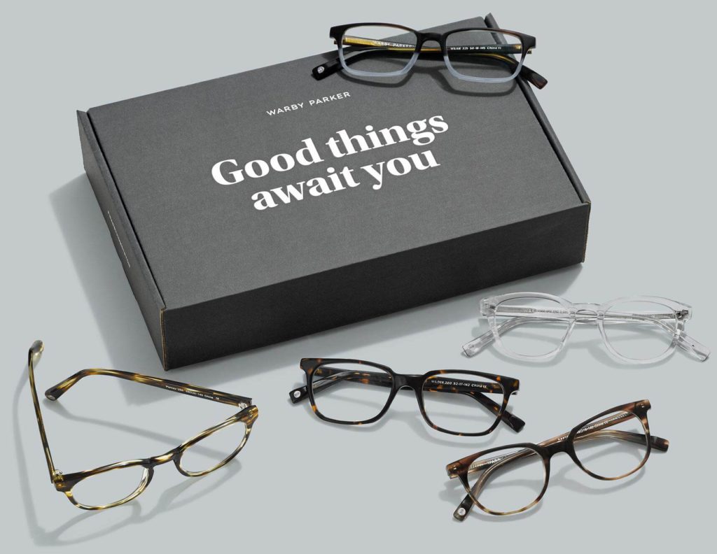 A range of eyeglasses arrange around a Warby Parker branded box.
